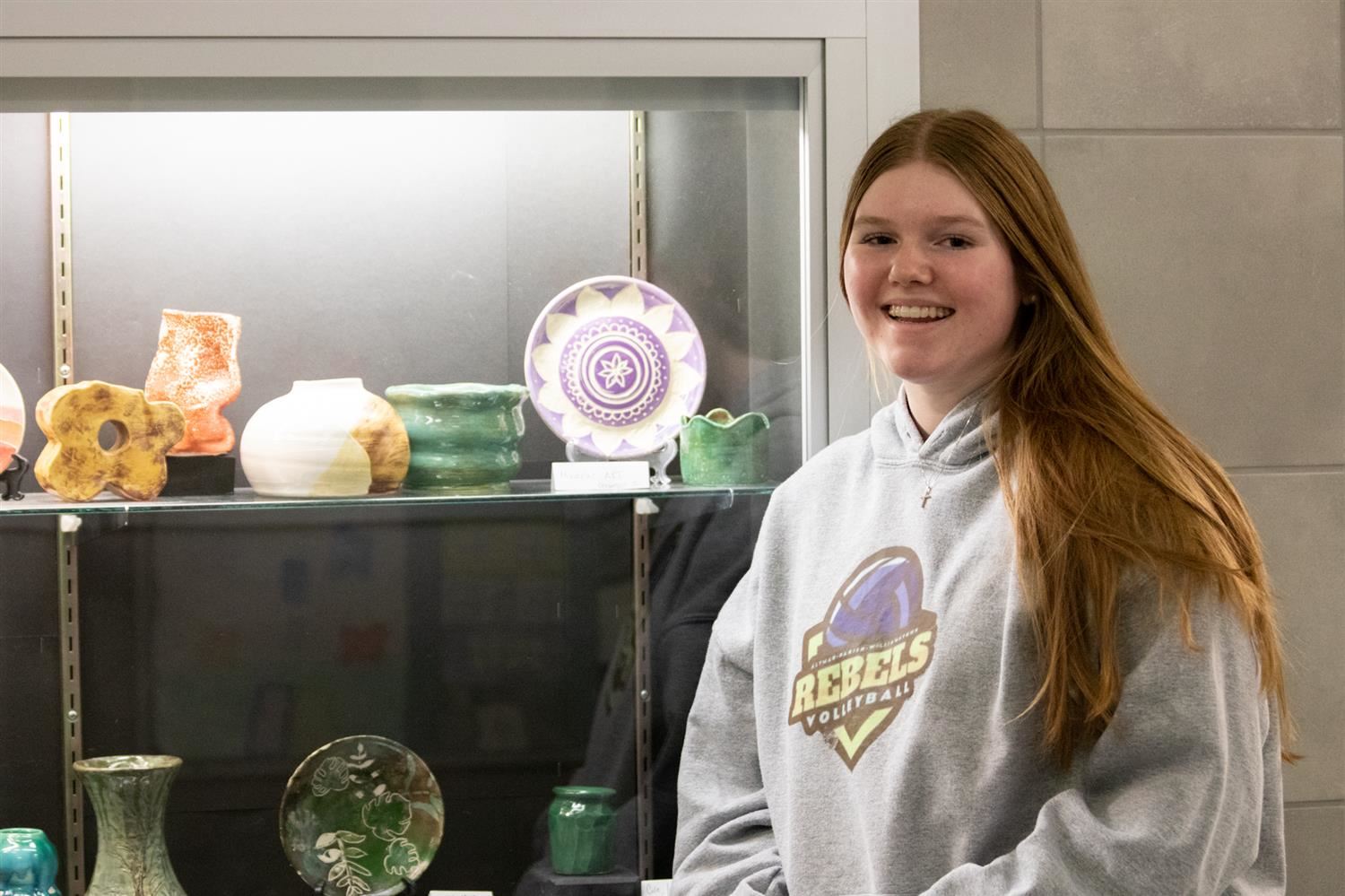  Senior Mikayla Mattison smiles in front of a cabinet of her work.